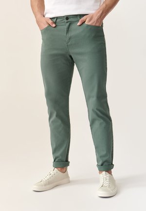 Pantaloni in denim verde con taglio slim, design a cinque tasche e risvolti, abbinati a sneaker bianche con lacci.