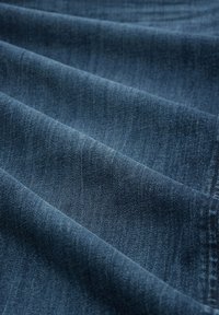Gros plan d'un tissu en denim bleu foncé avec texture visible et plis doux montrant le motif du tissage et les détails des coutures.