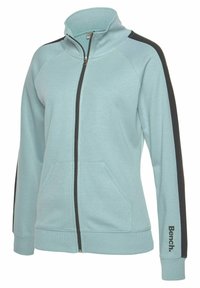 Helles blaues Zip-up-Jackett mit hohem Kragen, schwarzen Seitenstreifen, zwei Fronttaschen und "Bench."-Logo am linken Ärmel. Weicher Stoff.