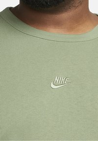 Světle zelené pruhované tričko s kulatým výstřihem a bílým výšivkovým logem Nike na hrudi. Měkká textura a přiléhavý střih.