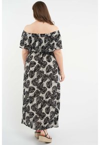 Mustassa ja valkoisessa off-shoulder maksi mekossa on lehtipainatus, röyhelöillä varustettu yläosa ja teksturoitu kangas. Espadrille-sandaalit näkyvät.