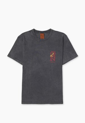Camiseta de algodón gris con cuello redondo, mangas cortas y un gráfico rojo de un pájaro y la letra "N" en el pecho izquierdo. Textura desgastada.
