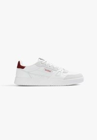 White sneaker featuring a leather and suede upper, round toe, flat white sole, and a red accent at the heel. Brand name displayed on the side.