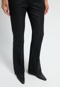 Zwarte flare jeans met een donkere wassing, gecombineerd met puntige zwarte hakken. Heeft een klassieke vijf-pocket ontwerp en een recht gesneden silhouet.