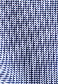 Blauw en wit houndstooth-stofpatroon met kleine, herhalende geometrische vormen die een gestructureerde uitstraling creëren.