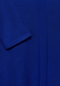 Tessuto blu lavorato a maglia con un motivo strutturato, cucitura visibile e dettaglio della manica piegata. Texture morbida e punti uniformi.