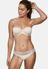 Soutien-gorge sans bretelles en dentelle beige avec un motif floral et un petit nœud au centre; culottes hipster en dentelle transparente assorties, tissu lisse, design minimaliste.