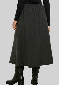 Temno siva, široka maxi krila s elastičnim pasom, izdelana iz teksturiranega blaga. Nošena s črnimi čevlji do kolen.