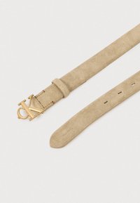 Beigenvärinen mokkanahkainen vyö, jossa on kultainen metallisolki, jossa kirjaimet "CK." Vyössä on sileä pinta ja useita säätöreikiä.