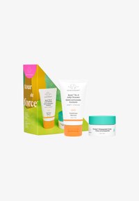 Drunk Elephant skincare set in a triangular green box. Includes a white cleanser tube with orange accents and two cream jars with teal lids.