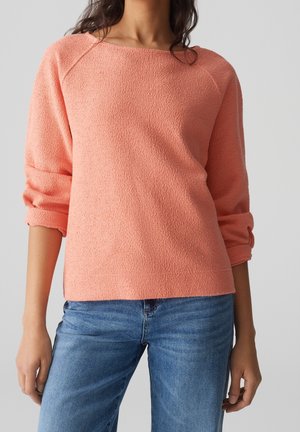 Koralfarbenes, strukturiertes Sweatshirt mit Dreiviertelärmeln und weitem Ausschnitt, kombiniert mit blauen Jeans. Weicher Stoff, lässige Passform.