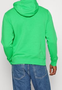 Grön huvtröja med dragsko i huven, ribbade ärmslut och midja, tillverkad av bomullsblandat tyg. Buren med ljusblå denimjeans.
