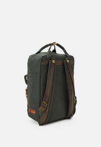 Sac à dos vert foncé en tissu résistant. Il comporte des bretelles marron, une poignée supérieure, et une poche latérale avec des accents et boutons en laiton.