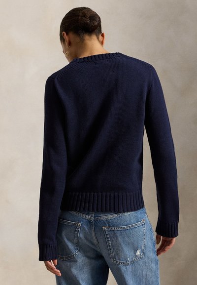 Navy knit sweater with a ribbed hem and cuffs, featuring a textured finish and a round neckline. Paired with light blue distressed jeans.