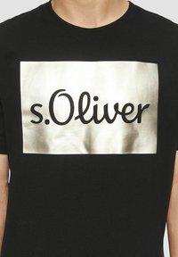 Schwarzes Baumwoll-T-Shirt mit einem glänzenden goldenen Rechteckdruck, auf dem der Text "s.Oliver" in fetter schwarzer Schrift steht. Kurze Ärmel und runder Ausschnitt.