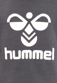 Szary materiał z dużym białym wzorem graficznym przypominającym pszczołę, z tekstem "hummel" poniżej. Gładka tekstura o swobodnym wyglądzie.