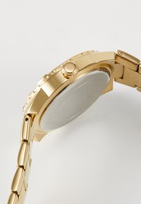 Montre-bracelet en métal doré avec un boîtier rond, couronne visible et bracelet à maillons. La finition de surface lisse et la texture polie mettent en valeur le design.