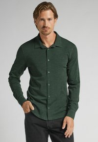 Mörkgrön rutig skjorta med lång ärm och platt krage, som har en subtil textur och standard knappstängning, i kombination med svarta byxor.
