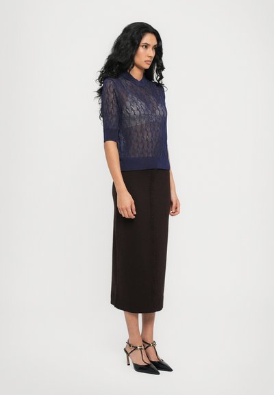 Top de punto azul marino de manga corta con un patrón texturizado, combinado con una falda marrón hasta la rodilla con botones en el frente y zapatos de tacón negro.
