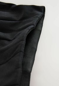 Tissu noir à la texture lisse et au design froncé. Doté d'un bandeau élastique sur le bord, offrant un aspect ajusté.