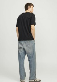 Sort bomulds T-shirt med korte ærmer, parret med lyseblå, løstsiddende denimjeans. Enkel design, robust stof, minimal detaljer.