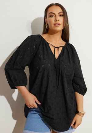 Tunique noire avec une coupe ample, des manches ¾, un décolleté en V avec un lien à nouer, et des motifs de broderie géométrique sur le tissu.