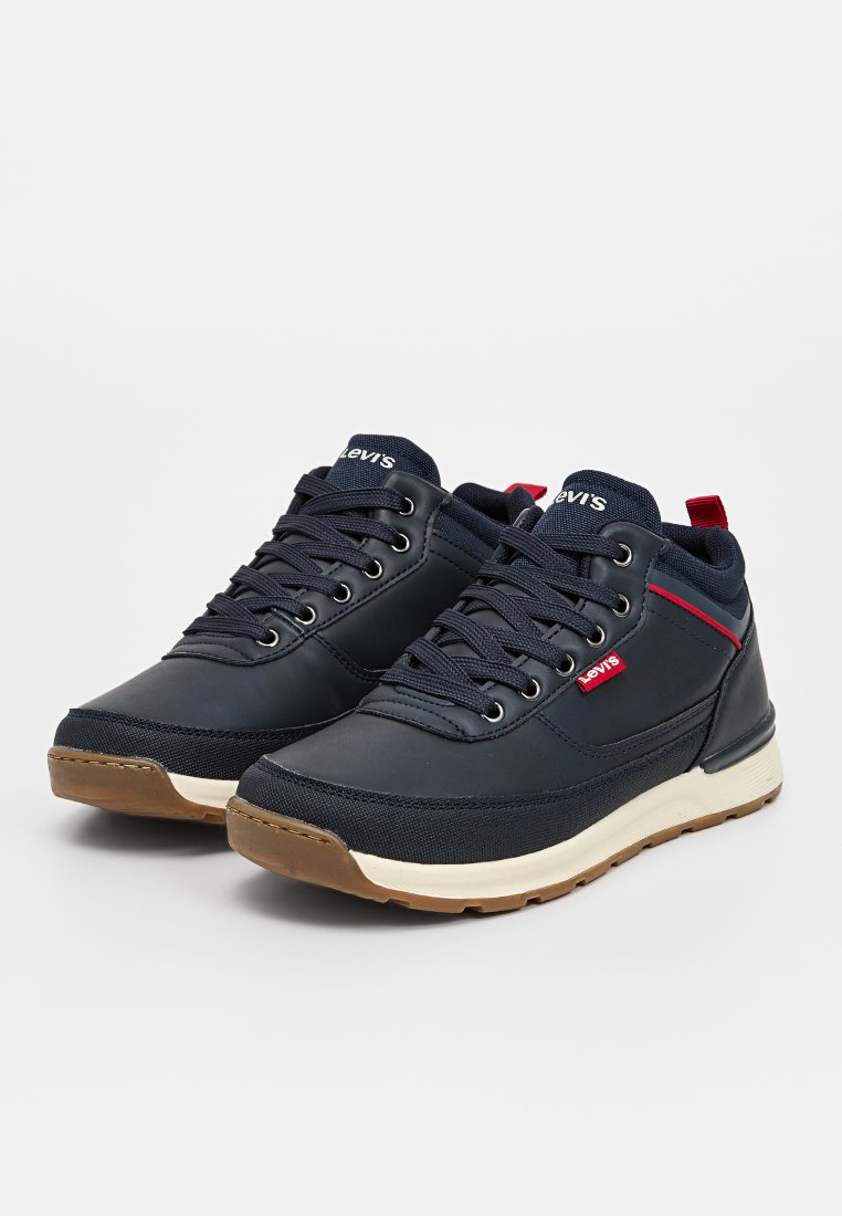 Baskets de sport navy avec un mélange de matériaux synthétiques lisses et texturés, dotées de lacets ronds, d'une semelle intermédiaire blanche et de touches de rouge.