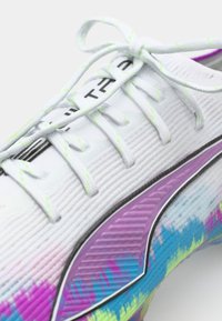 White athletic shoe with textured upper. Features colorful gradient design in purple, blue, and yellow. Includes flat laces and black accents.