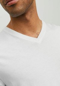 Witte katoenen V-hals T-shirt met een zachte textuur, met een relaxte pasvorm en minimale stiksels, weergegeven vanuit het perspectief van de hals en schouder.
