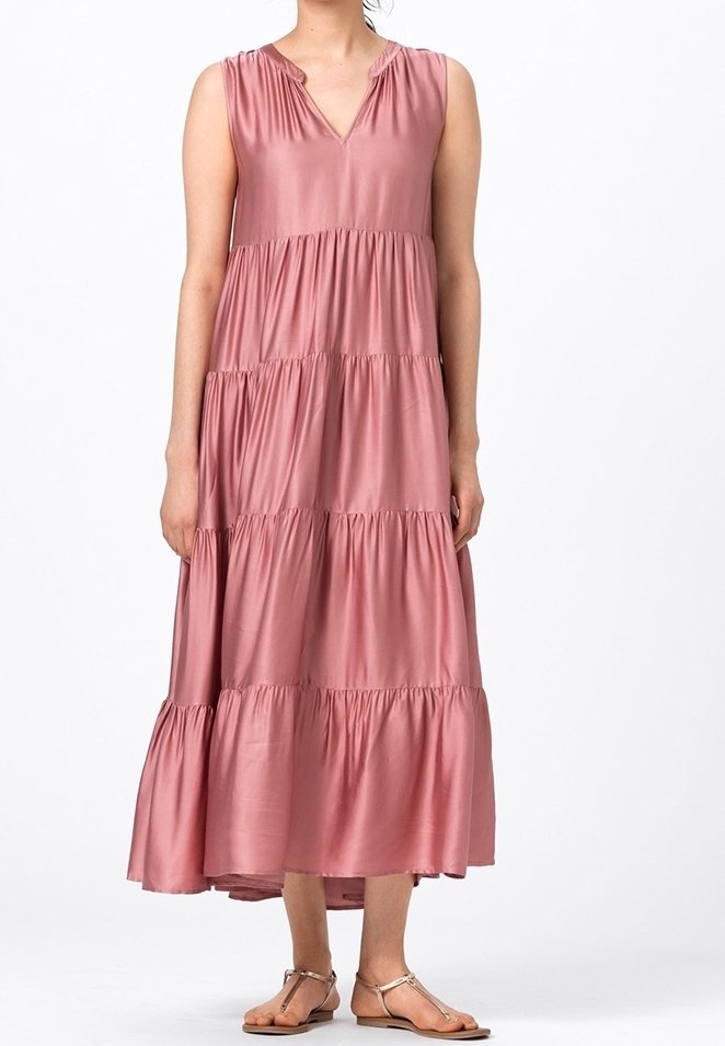 Robe longue rose poussiéreux à volants sans manches avec un décolleté en V, portée avec des sandales plates métalliques sur une personne debout, sur fond blanc.