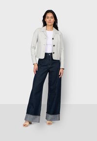Helles graues, tailliertes Jacket mit spitzem Kragen und drei runden Knöpfen, kombiniert mit hochgeschnittenen, weit geschnittenen dunklen Jeans mit umgeschlagenen Bündchen.