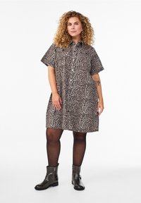 Šaty s leopardím vzorem, krátkými rukávy, zapínáním na knoflíky vpředu a uvolněným střihem. Nositý s černými kotníkovými botami a průhlednými černými punčocháči.