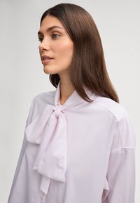  Lichtroze blouse met een strik om de kraag, lange mouwen en knoopdetails, gemaakt van gladde stof, met een ontspannen pasvorm en een zachte textuur.
