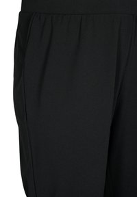 Schwarze Stretchhosen mit glatter Textur, elastischem Bund und Seitentaschen. Das Design bietet sanfte Drapierungen für Komfort und Bewegungsfreiheit.