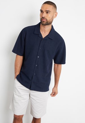 Navy short-sleeve button-up shirt with a textured fabric, a pointed collar, and front buttons, paired with white shorts.