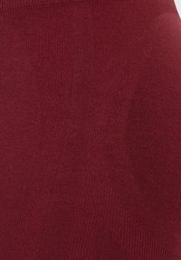 Bordeaux leggings van een getextureerde gebreide stof met verschillende patronen: een gladde zone en een ribbelsectie.