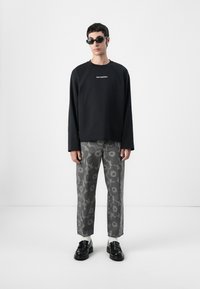 Felpa nera a maniche lunghe con logo bianco, abbinata a pantaloni larghi grigi a fantasia e mocassini neri con accenti bianchi.