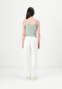 Lysegrønn stripete tank topp med tynne stropper, parret med løstsittende hvite bukser og hvite joggesko, sett fra baksiden.