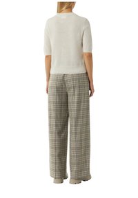 Hellbeige Kurzarm-Pullover mit weicher Textur, kombiniert mit weiten, karierter Hose in Cremetönen, Braun und Blau, dazu neutrale Stiefel.