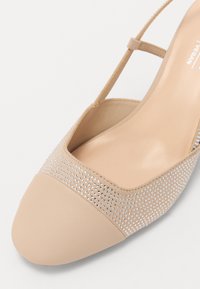 Beige veganská kožená bota s kulatou špičkou, která má třpytivý akcent z rhinestone a jemný pásek kolem kotníku. Hladké a texturované povrchy.