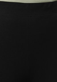 Leggings noirs en tissu doux et extensible. Ils disposent d'une large taille élastique de couleur vert clair avec une texture côtelée.