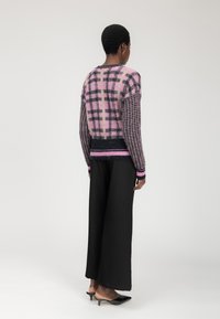 Maglione a maglia con un motivo scozzese rosa e nero, caratterizzato da un design a punto aperto testurizzato, polsini a costine e un orlo in contrasto. Pantaloni larghi neri.