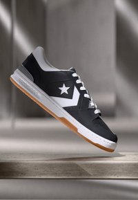 Black leather sneaker with white accents, a star logo, and gray details. Features a rubber sole with a gum color and white laces.