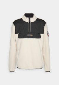 Fleece-pullover i crème med svart nylonpanel. Kvartdragkedja, bröstficka och logotyp patch på ärmen. Mjuk textur, kontrasterande färger.