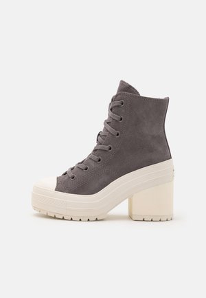 Bota ankle cinza em camurça com biqueira de borracha branca e salto chunky bege. Apresenta atacadores e um superior texturizado.