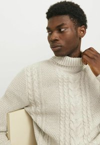 Suéter de punto beige con cuello alto acanalado y patrón texturizado, con acentos de acanalado vertical y horizontal.