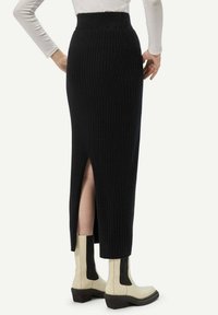 Jupe en maille côtelée noire avec une fente sur le côté et une taille haute, associée à des bottines crème avec des accents noirs.