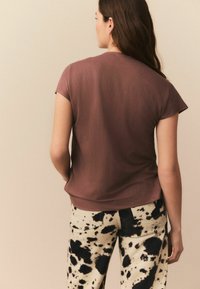 Korte mauve T-shirt van zachte stof, gecombineerd met beige broek met een zwart gepunte patroon. Ontworpen met korte mouwen.