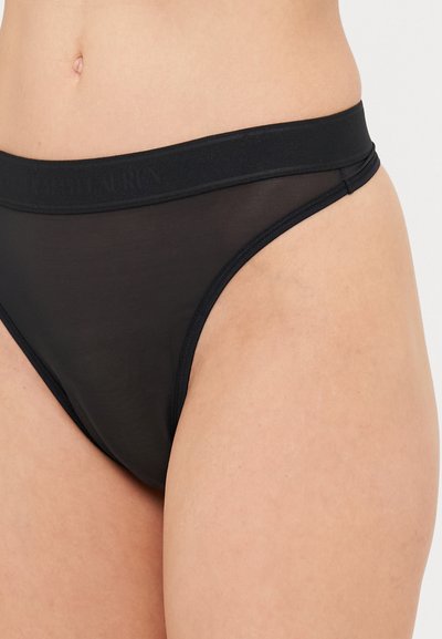 Melns tanga apakšveļa ar plašu, mīkstu jostu, uz kuras ir viegli pamanāma logo. Materiāls ir caurspīdīgs un gluds, ar vienkāršu griezuma dizainu.
