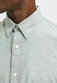Lichtgroene, gekraagde shirt van textuurstof met een voorste knoopsluiting met witte knopen en een subtiele linnen uitstraling.